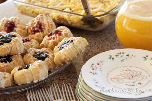Blackberry and Cherry Kolaches with a large glass of Orange Juice and a large egg casserole in background