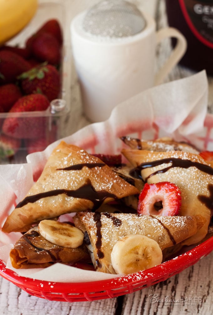 Baked Nutella turnovers - phyllo dough wrapped around a sweet, creamy, chocolaty Nutella cream cheese filling baked until it's crispy, flaky, and golden brown then served with sliced strawberries and bananas, drizzled with chocolate and sprinkled with powdered sugar. 