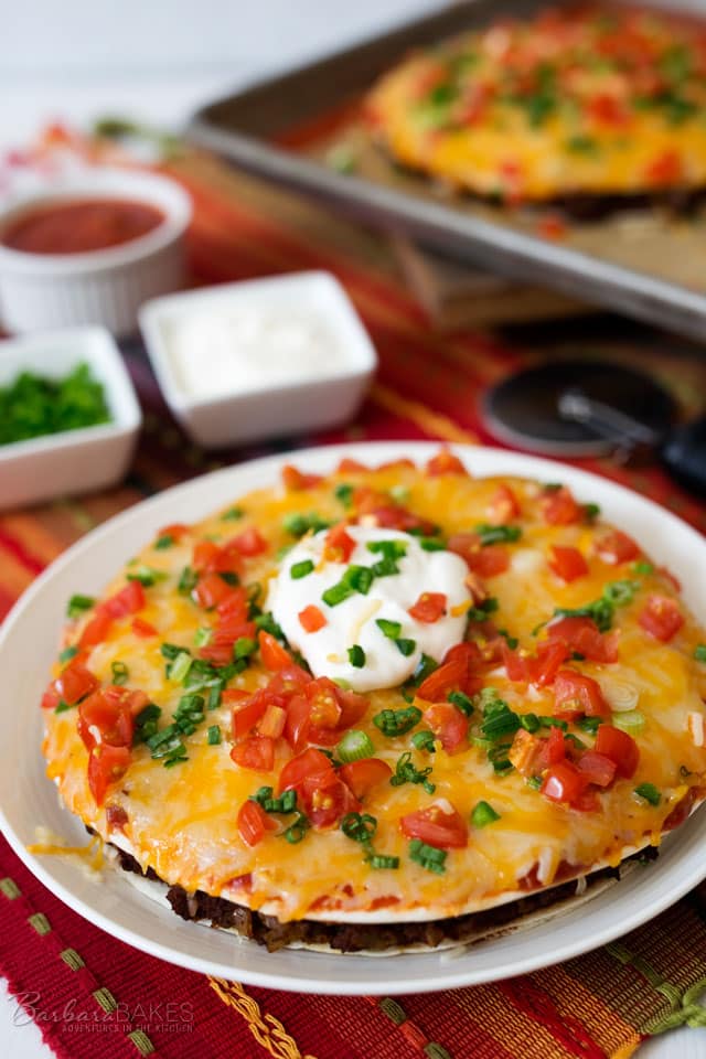 A fun Mexican Pizza with a layer of refried beans and spicy ground beef sandwiched between two flour tortillas, topped with salsa, shredded cheese, jalapenos, green onions, and tomatoes. Then baked until it's hot, melty and gooey delicious.
