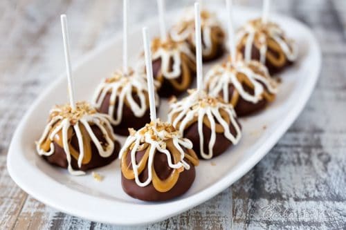 A serving tray filled with eight brownie pops, dipped in chocolate and drizzled with caramel and white chocolate