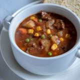 Round steak beef stew with colorful vegetables in a white bowl