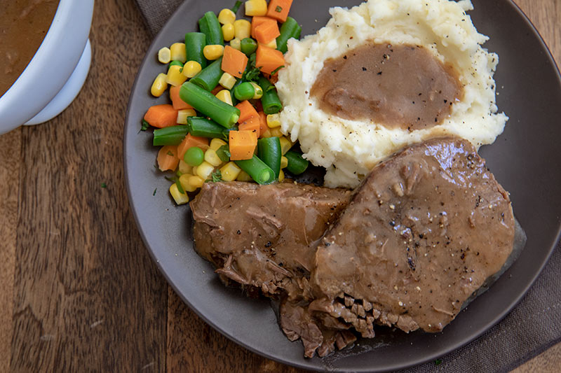 Round Steak with Mashed Potatoes and Gravy ready to be served on a gray plate