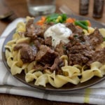 A plate of pasta topped with round steak in gravy and a dollop of sour cream.