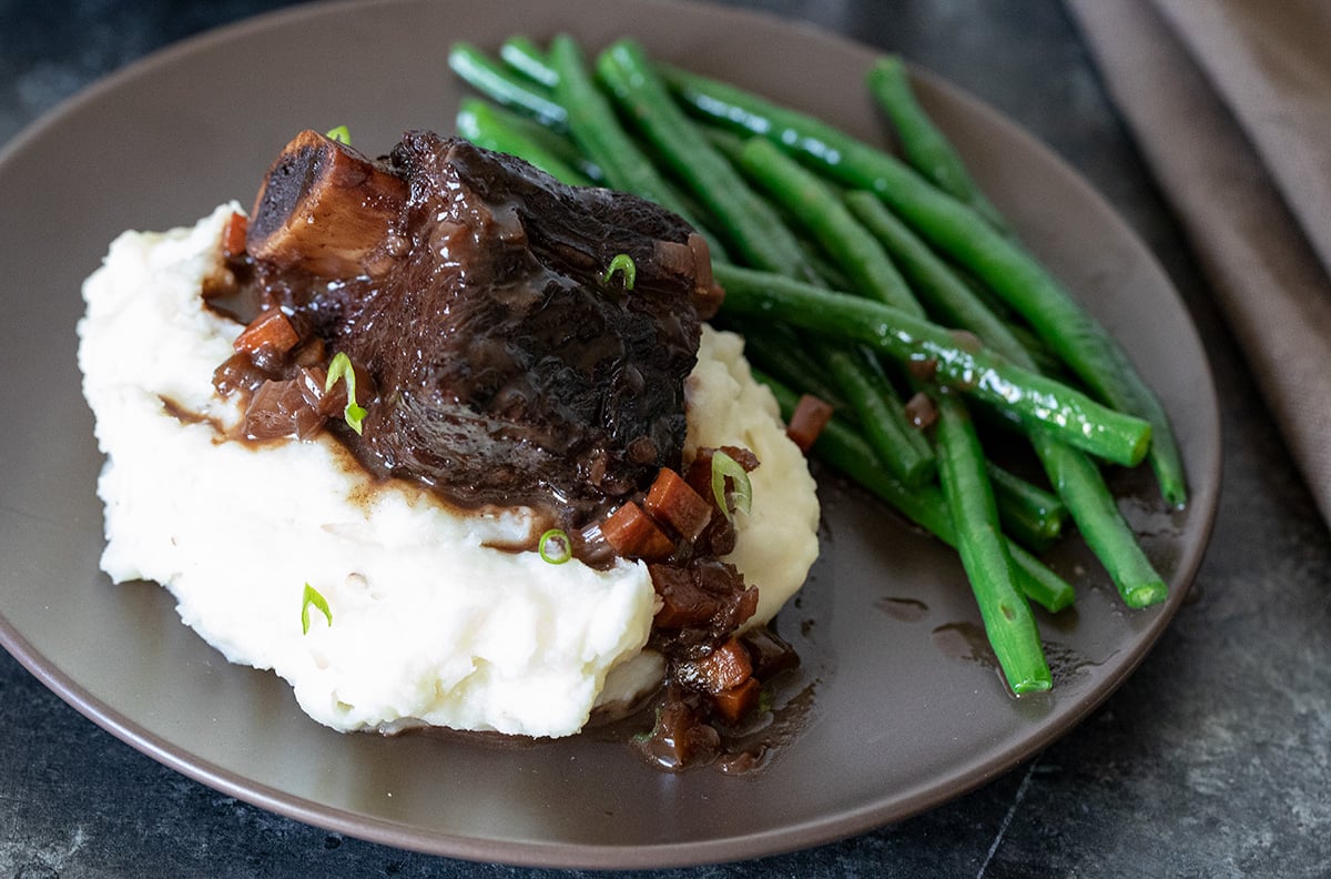 closeup of braised beef short ribs on a plate with mashed potatoes and green beans