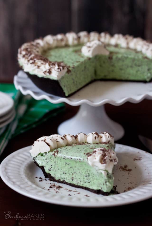 Mint Chocolate Chip Pie served on a white plate with rest of pie in background on a cake stand