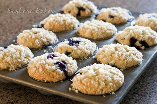 a muffin tin with 12 blueberry muffins topped with struesel