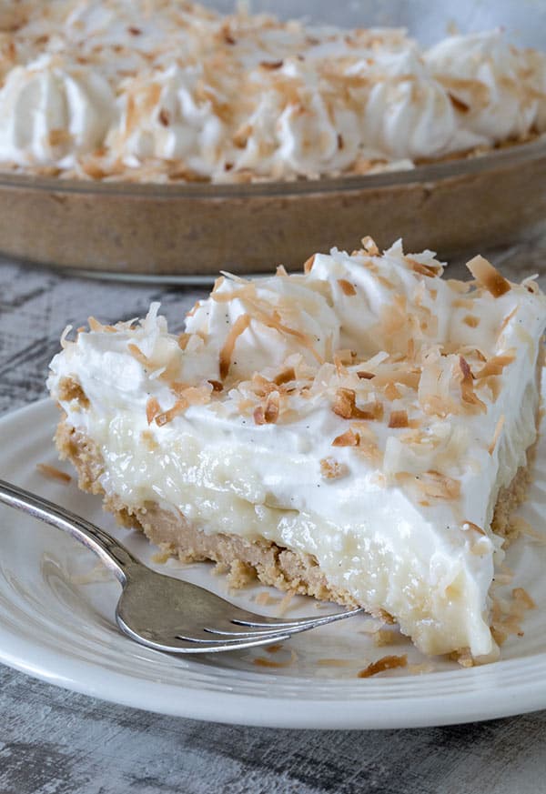 A slice of Coconut Cream Pie in a Shortbread Crumb Crust served on a white plate with a fork