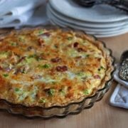 quiche in a pan with serving utensils and stacked plates