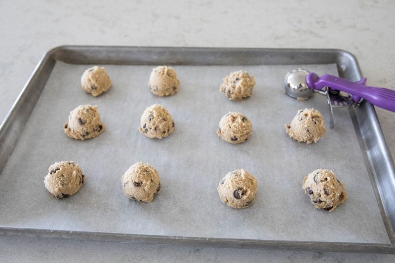 Cookie dough balls arranged on a cookie sheet and a #40 disher