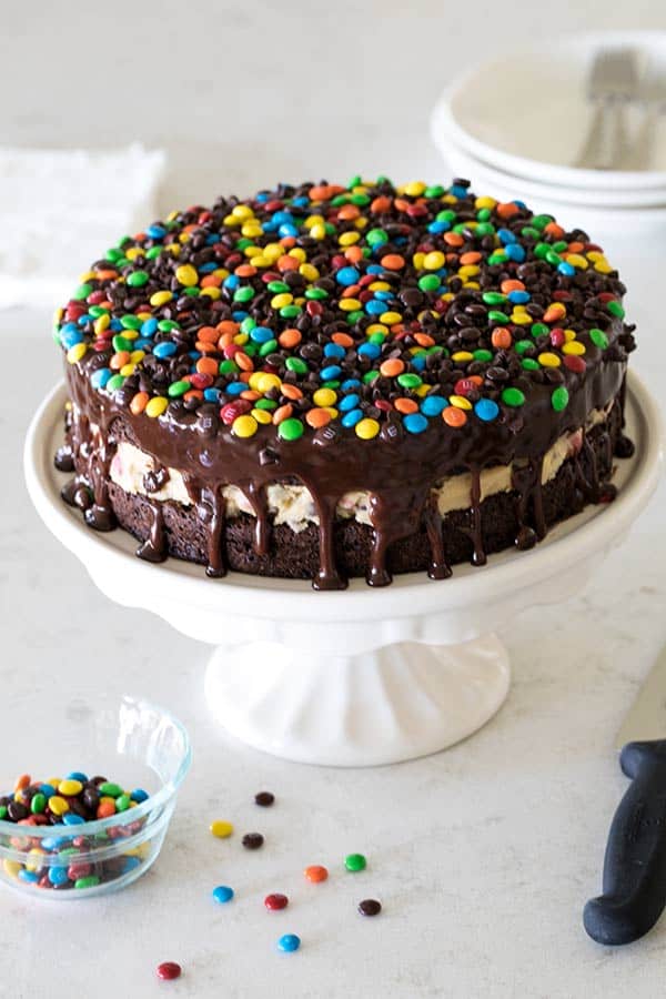 M&M Cookie Dough Brownie Bomb Cake on a white cake stand