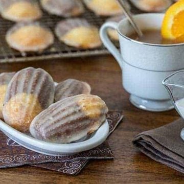 Glazed Chocolate Orange Marbled Madeleines on a white plate with a cup of tea