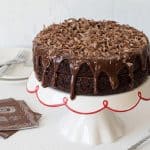 A Triple Chocolate Layer Cake drizzle with rich milk chocolate ganache and topped with shaved chocolate curls.
