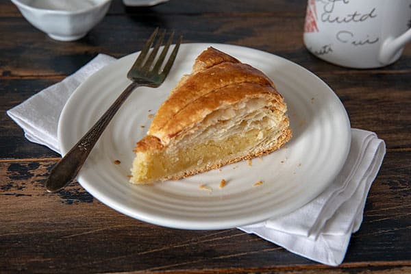 Sliced Pithivier pastry on a white plate with a fork and served with a cup of coffee