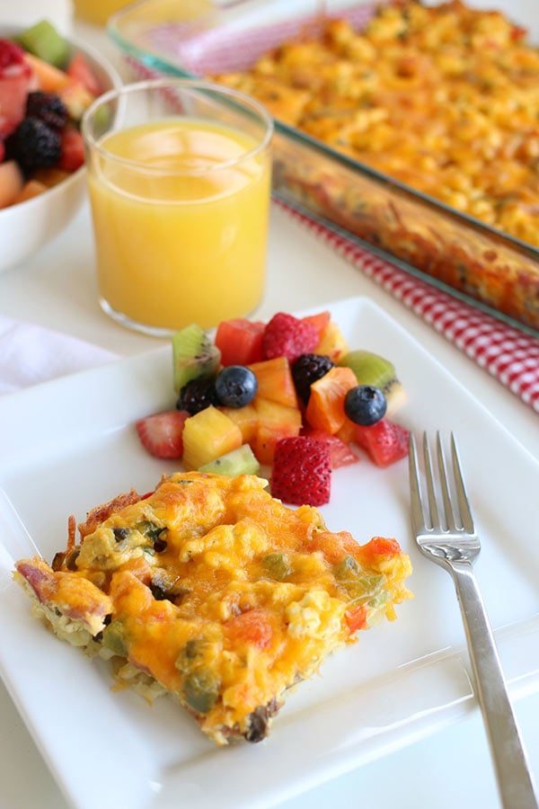 A plate of Breakfast Hashbrown Casserole with mixed fruit and a glass of juice