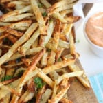 Air fryer french fries sitting next to a cup of dipping sauce