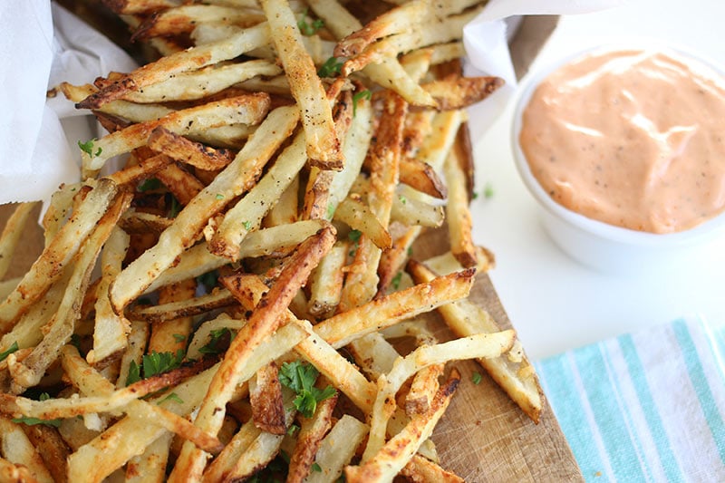 Air fryer french fries sitting next to a cup of dipping sauce