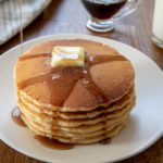 Pancakes with a dollop of butter and maple syrup served on a white plate