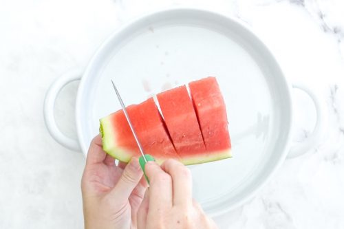 a triangle of watermelon held by the rind and sliced into strips to make watermelon cubes