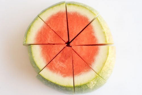 a watermelon on a cutting board sliced into thick wedges with the rind
