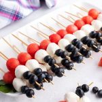 Red, White and Blue Fruit and Cheese skewers on a white platter with springs of mint