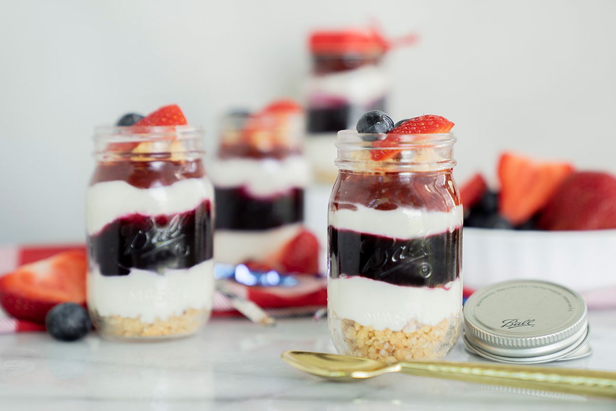 several no-bake red white and blue min i cheesecake in mason jars with fresh berries on top