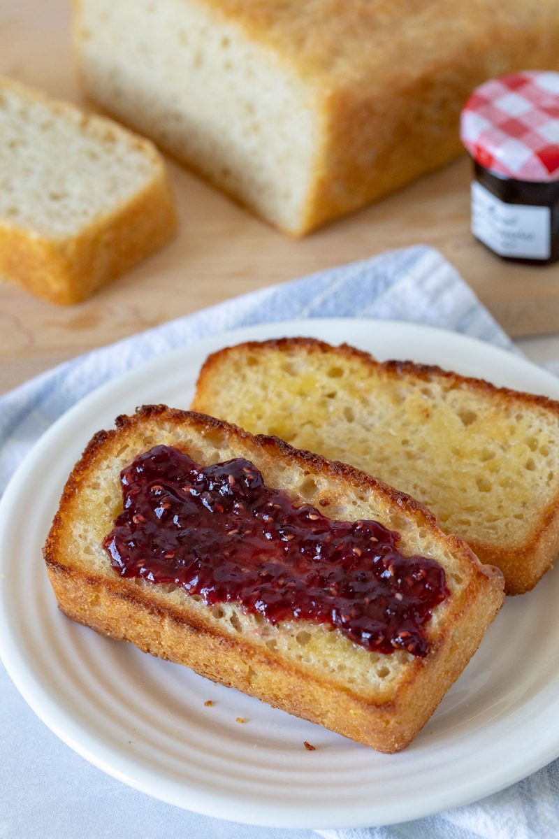 Two slices of English muffin bread, one with jam, on a white plate.