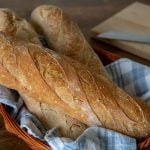 Three small loaves of French bread in a basket with a blue and white napkin