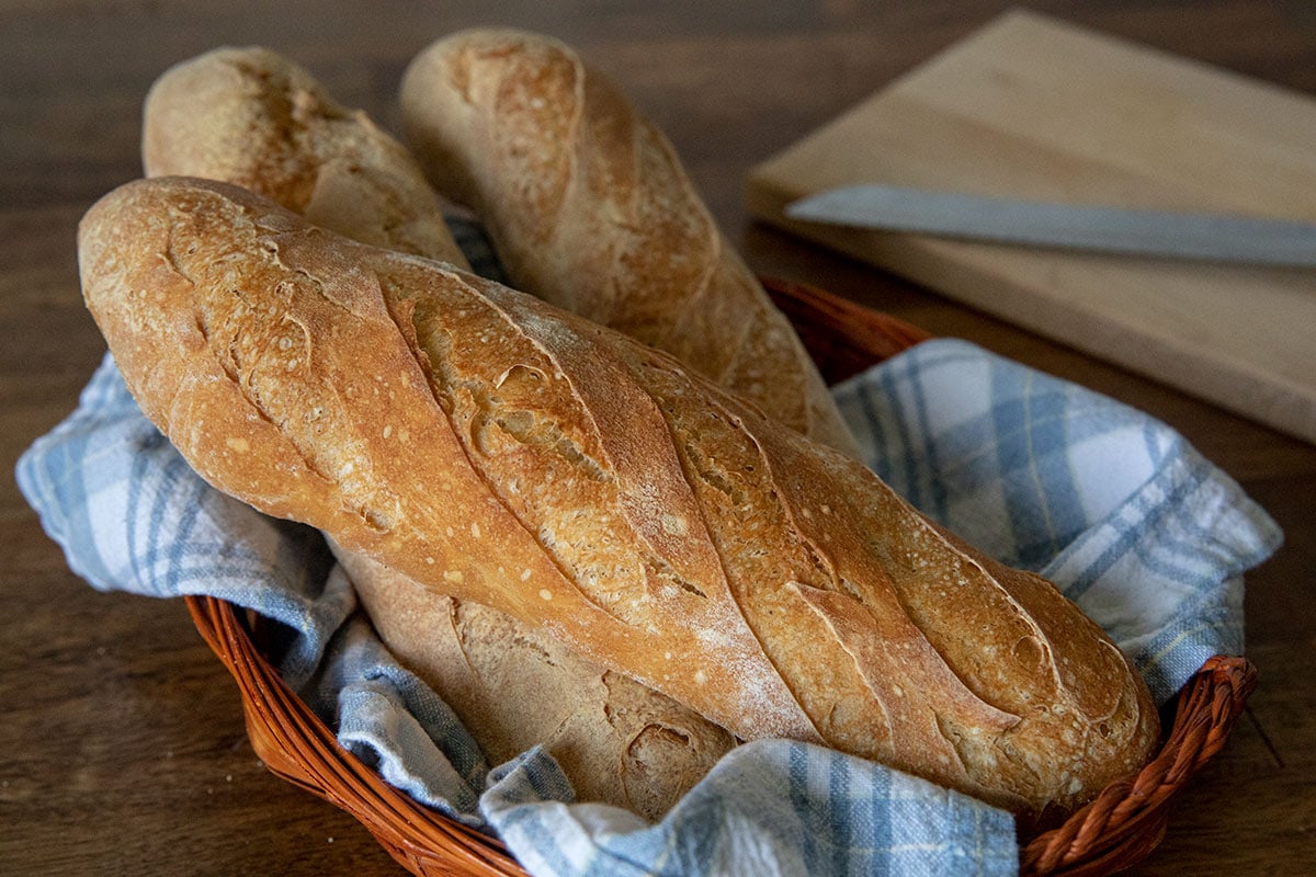 Three small loaves of French bread in a basket with a blue and white napkin