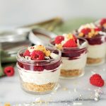mini mason jars filled with white chocoalte raspberry cheesecake and fresh raspberries lined up on a marble counter