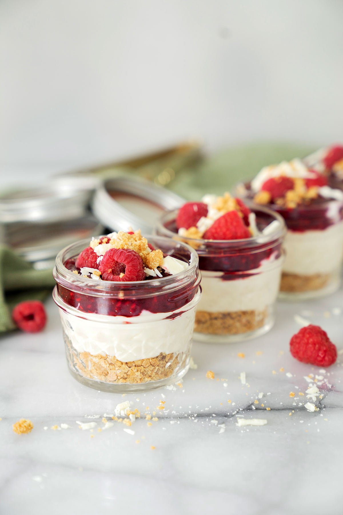 mini mason jars filled with white chocoalte raspberry cheesecake and fresh raspberries lined up on a marble counter