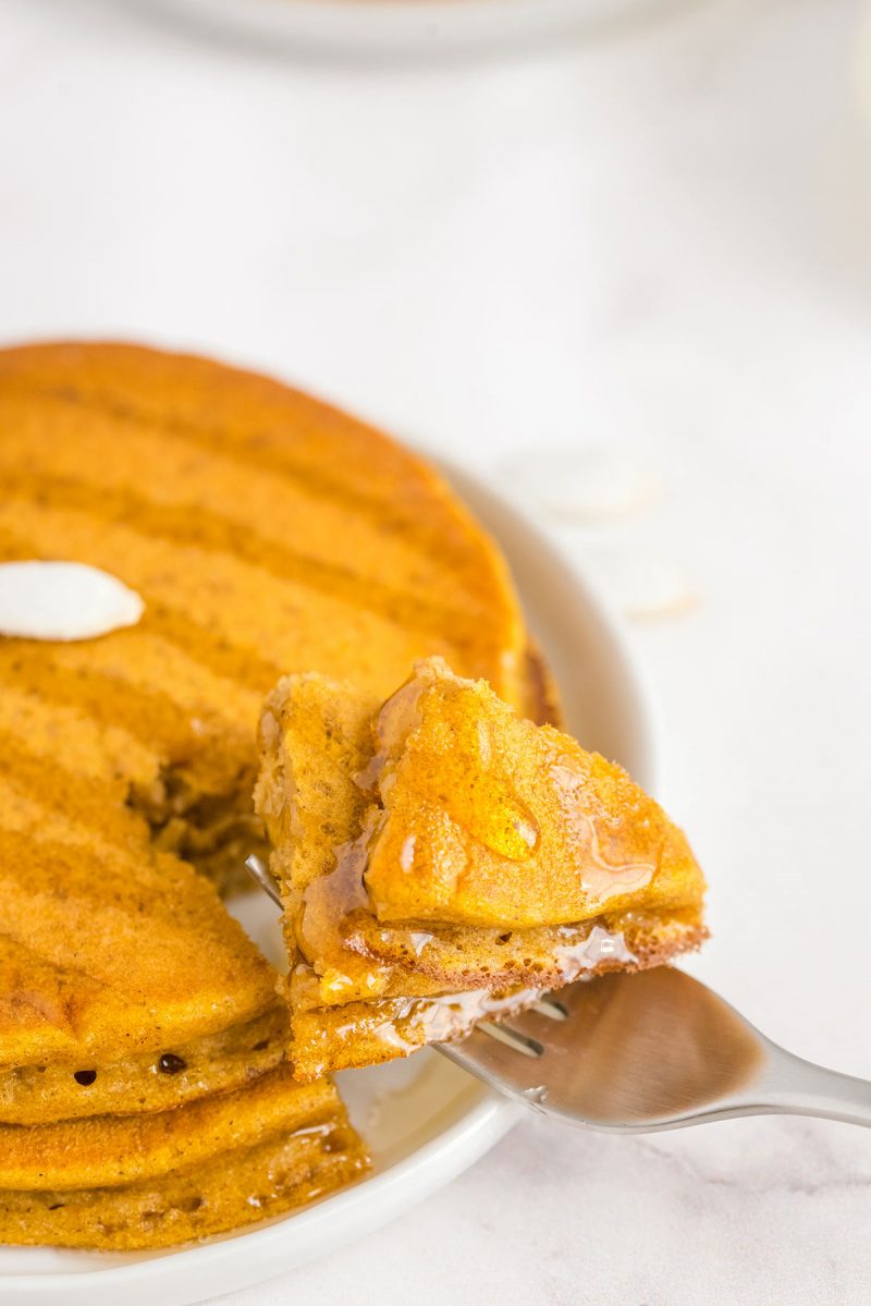 taking a bite of a stack of fluffy pumpkin pancakes with butter and maple syrup