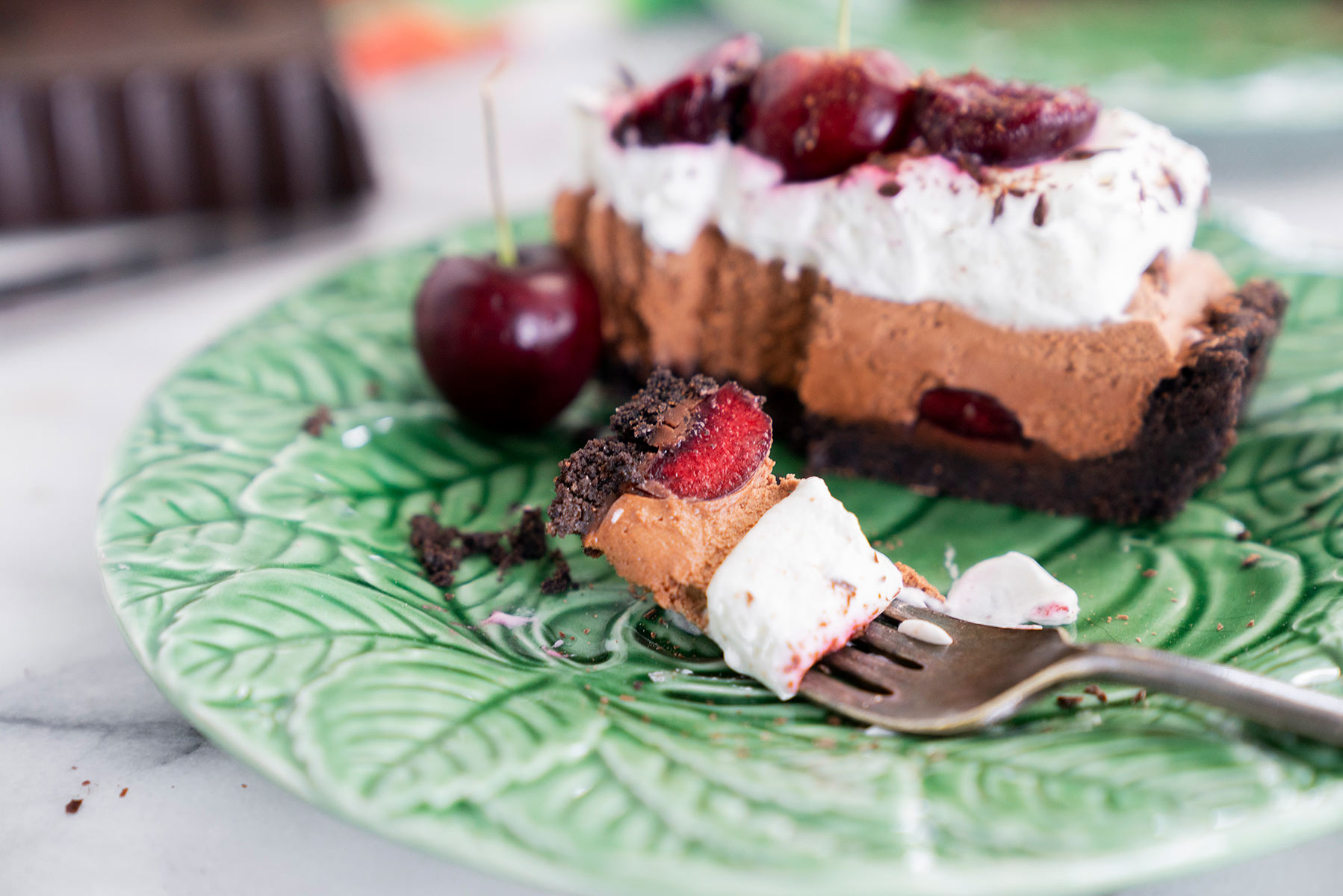 slice of black forest tart with fresh cherries and whipped cream with a bite taken out on a green plate