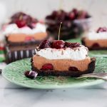 slice of black forest tart with whipped cream and a fresh cherry on top on a green dessert plate