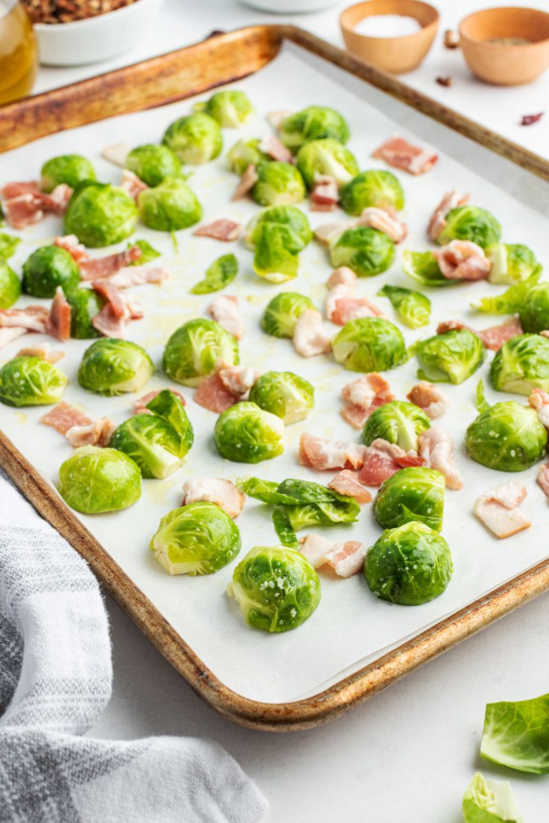 uncooked brussel sprouts on a baking sheet with bacon pieces