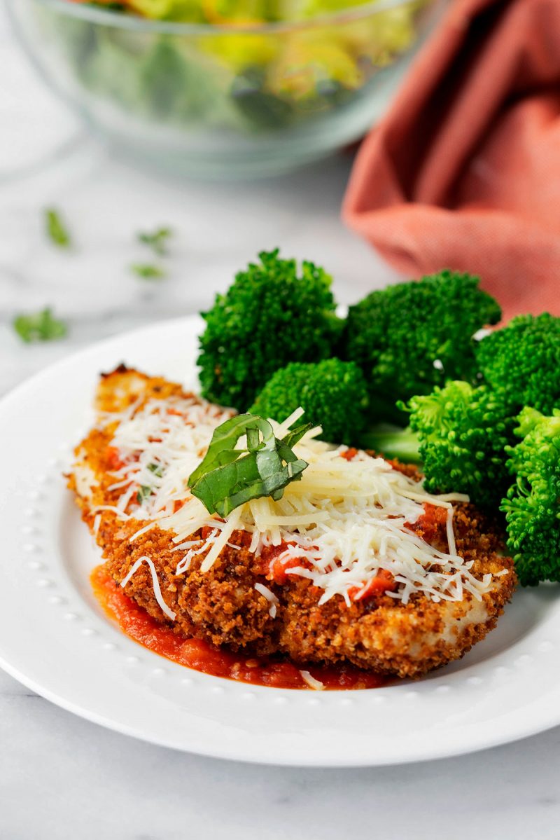 light chicken parmesan with steamd broccoli on a white dinner plat