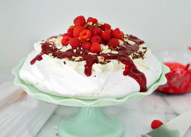 side view of pavlova with raspberries and white chocoalte whipped cream on a green cake stand