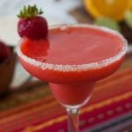 glass with a frozen strawberry margarita, a sugar rim and fresh berry on the side