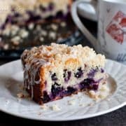 Lemon blueberry coffee cake with streusel topping over white icing, one slice on a white plate