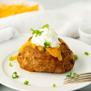 baked air fried potato on a white plate with cheese, sour cream and scallions