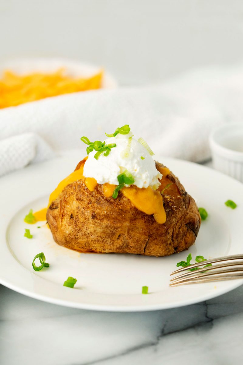 baked air fried potato on a white plate with cheese, sour cream and scallions