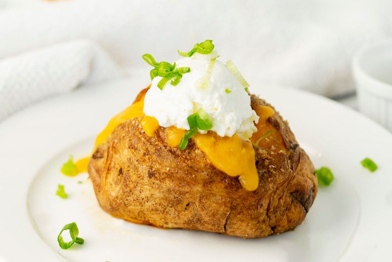 white plate with a baked potato with sour cream, cheese and scallions
