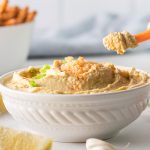 white bowl of homemade hummus with a carrot stick dunked in