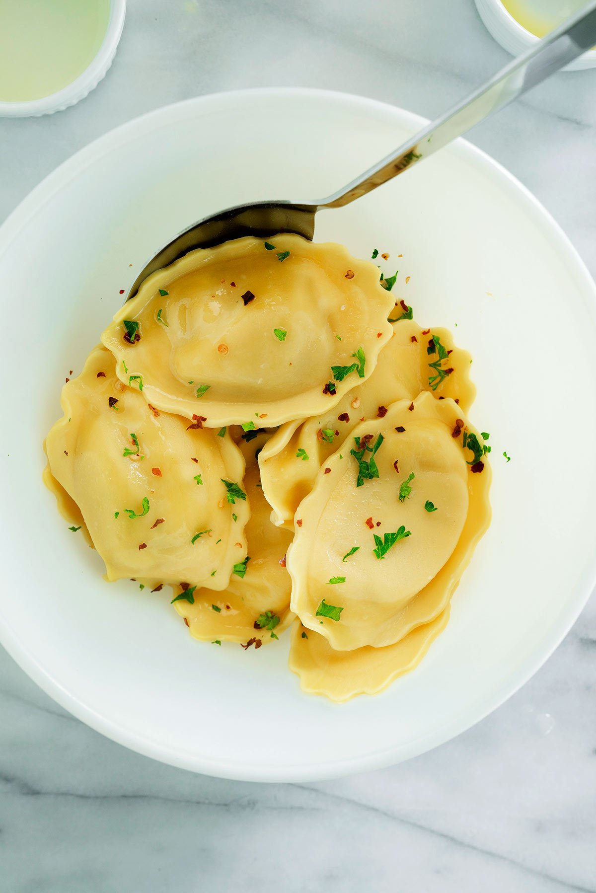 overhead of a white plate with ravioli, olive oil and herbs