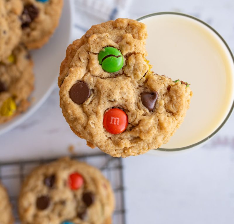 close up of a monster cookie with a bite out of it sitting atop a glass of cold milk