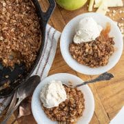 two plates with apple crisp and white ice cream with the cast iron baking dish next to them