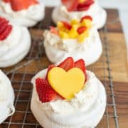 close up of strawberries and a yellow mango heart top fluffy bakes meringue on these pavlova bits on a cooling rack