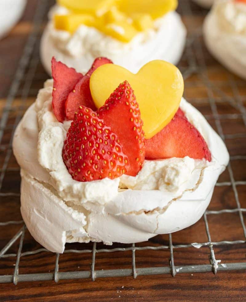 Strawberries and a yellow mango heart top fluffy bakes meringue on these pavlova bits on a cooling rack