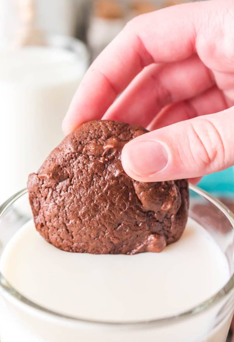 puffy double chocolate cookie being dipped into a glass of milk