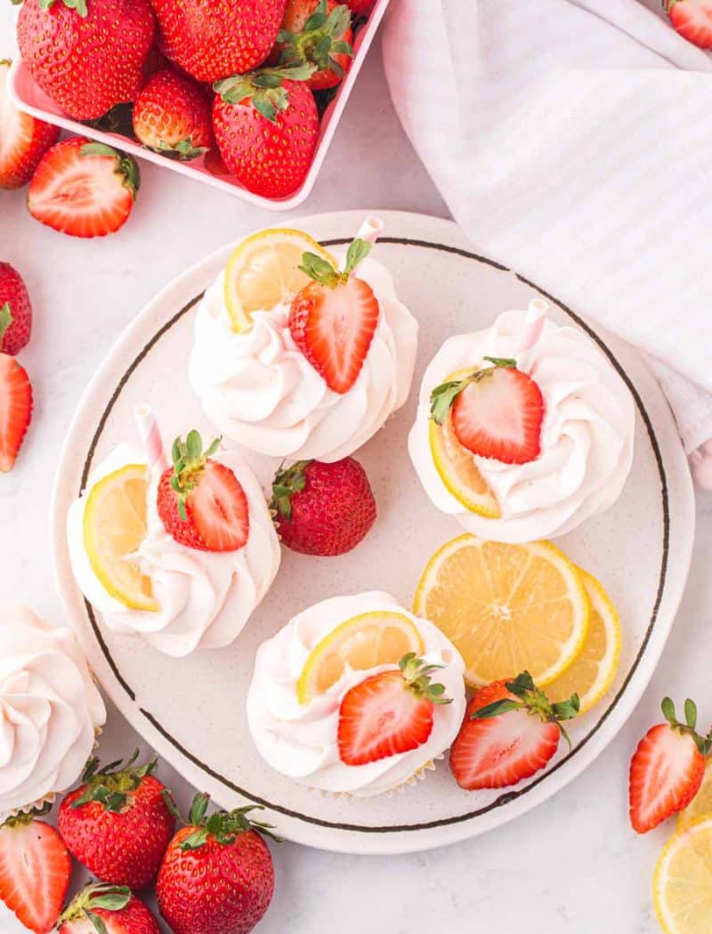 white plate with lemon strawberry cupcakes, adorned with fresh lemon and strawberries