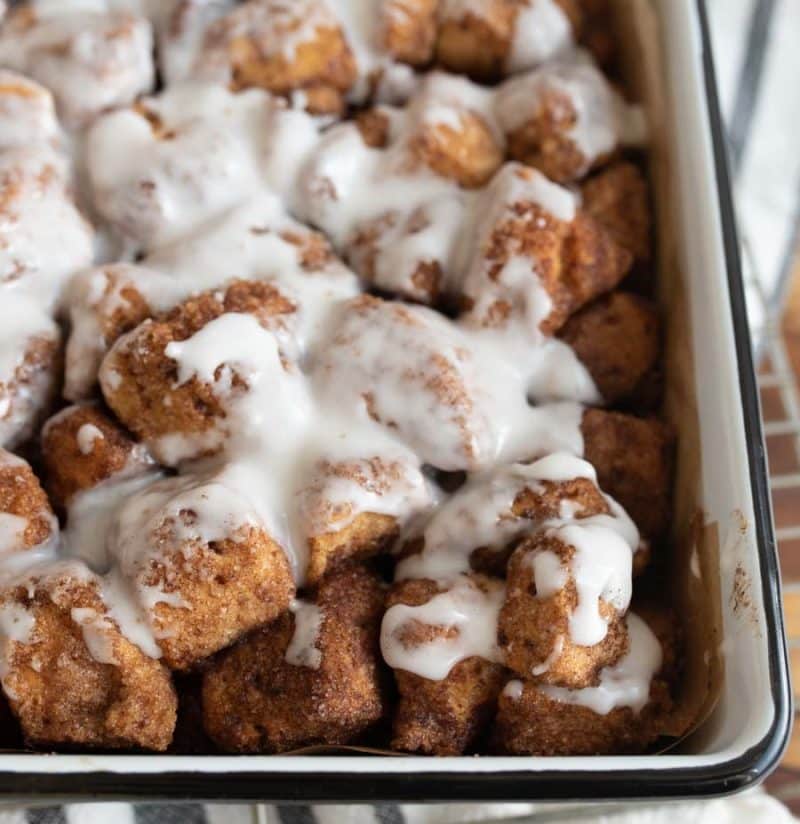 close up cinnamon roll casserole bits baked into a dish with icing